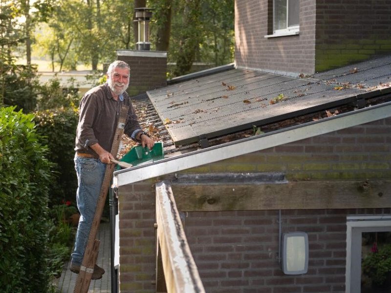 Jan Schreurs staat op een ladder en veegt de bladeren van zijn zonnepanelen