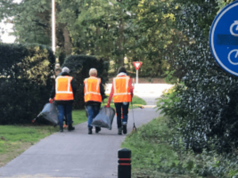 Drie mensen lopen met afvalzakken en -prikkers over een fietspad