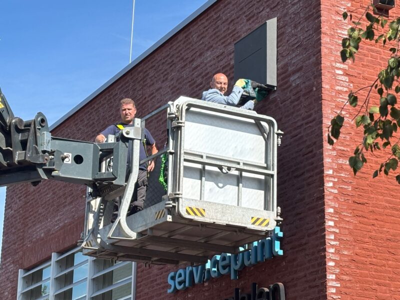 Wethouder Roland Slangen staat in een hoogwerker en boort een vleermuiskast tegen de gevel