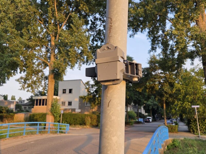 Klein kastje aan een lantaarnpaal met op de achtergrond huizen en bomen